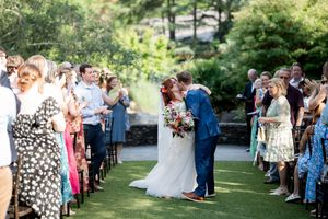 Bride and groom sharing first kiss at outdoor wedding ceremony surrounded by guests.