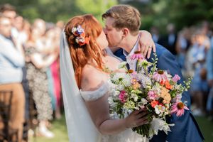 Close-up of bride and groom kissing, bride holding vibrant pink and orange floral bouquet.