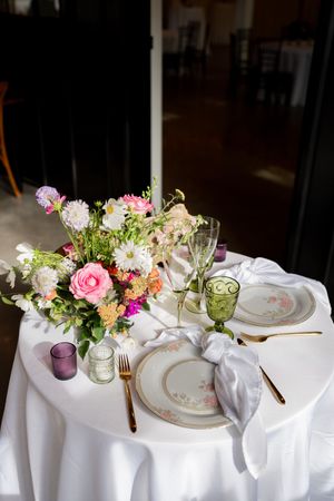 Elegant wedding table setting with floral centerpiece, gold cutlery, green glassware, and white linens.