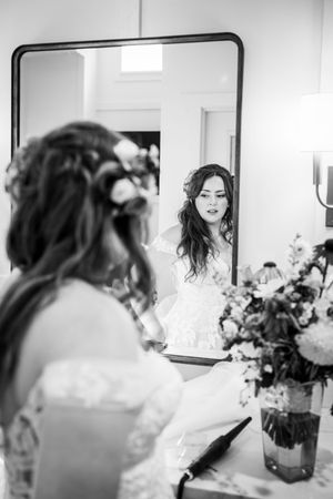 Black and white photo of a bride with floral crown reading vows while looking in a mirror during wedding prep.