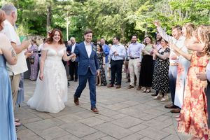 Bride and groom walk through cheering guests lining outdoor patio at wedding reception entrance.