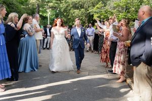 Newlyweds walk joyfully through cheering guests during outdoor wedding recessional on sunny day.
