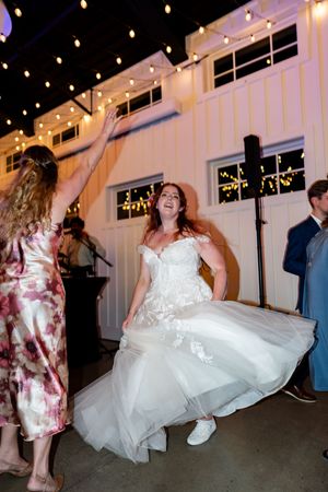 Laughing bride in a lace wedding gown twirling on the dance floor under string lights at her wedding reception.