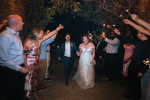 Joyful newlyweds walking through a sparkler exit tunnel surrounded by cheering wedding guests at night.