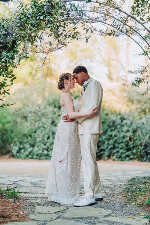 Newlyweds share an intimate forehead touch on stone path surrounded by lush greenery.