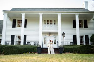 Couple embracing on steps of elegant white Southern colonial mansion with black shutters and grand columns.