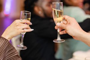 Two hands clinking champagne flutes at a celebration event, toasting with sparkling wine at a party.