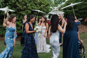 A group poses together with parasols at an outdoor event wearing elegant evening gowns in blue and floral patterns.