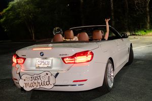 Newlyweds in a white BMW convertible with Just Married sign driving away at night.