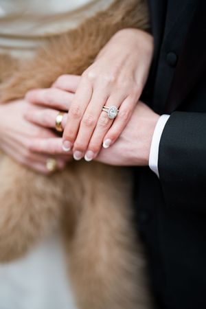 Close-up of bride's elegant oval diamond halo engagement ring and wedding band on her finger.
