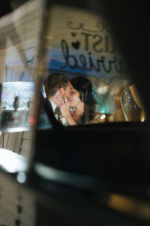 Newlyweds share a romantic kiss inside a vintage car decorated with a Just Married sign.