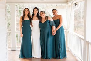 Bride poses with three bridesmaids in teal gowns on a white porch.