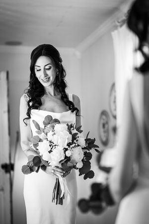 Black and white photo of smiling bride holding a white floral bouquet with eucalyptus.