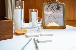 Elegant wedding date night jar station with candles, framed sign, and blank paper slips on white tablecloth.