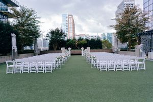 Rows of white folding chairs set up for an outdoor wedding ceremony on a green lawn with city buildings in background.