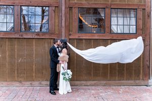 Bride and groom share a romantic kiss as her veil billows in the wind outside a rustic barn venue.