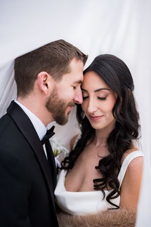 Bride and groom share an intimate forehead touch moment, bride in white gown with veil, groom in black tuxedo.