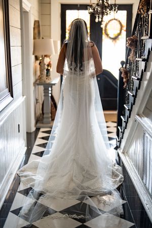 Elegant bridal veils hang in a row along a hallway with black railings and a crystal chandelier.