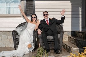 Newlyweds share joyful moments on outdoor porch steps during wedding photoshoot.