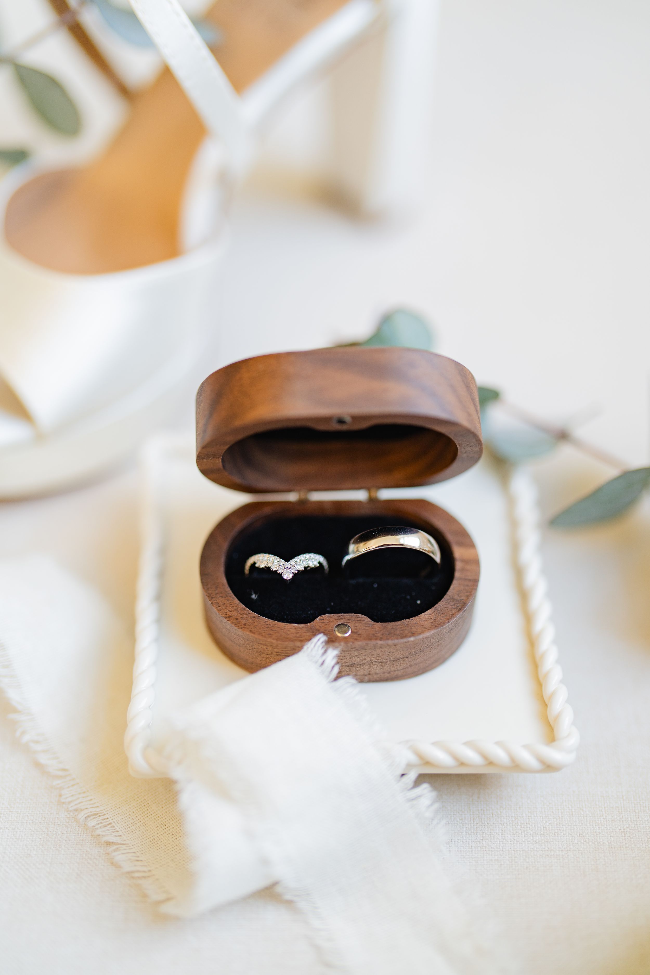 Wedding rings displayed in a wooden heart-shaped box lined with black velvet on a white cloth surface.