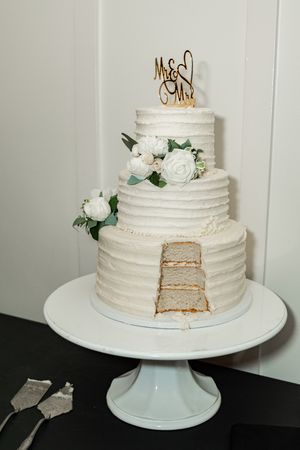 White wedding cake with rustic textured frosting and floral decorations shown from different angles on a pedestal stand.