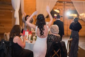 Bride in a fitted white gown raises her hands in celebration during the wedding reception.