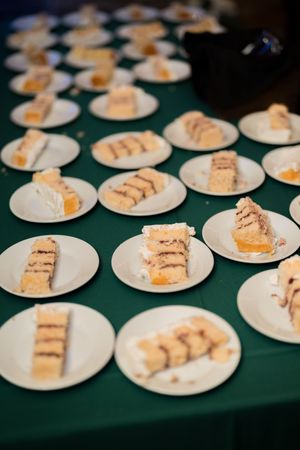 Multiple white plates with slices of layered cake arranged on a green tablecloth at a catered event.