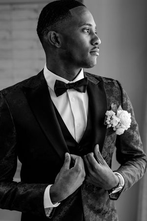 Elegant black and white portrait of groom in tuxedo with boutonniere looking to side in dramatic lighting.