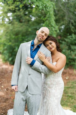 A couple in wedding attire embracing outdoors with greenery in the background.