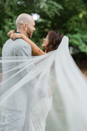 Romantic portrait of newlyweds with flowing veil in a garden setting.