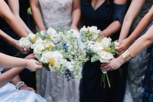 Multiple hands holding delicate white and blue floral bouquets together.