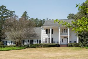 Large white colonial home with tall pillars, shuttered windows, and manicured lawn surrounded by mature trees.