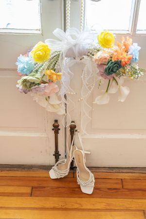 Colorful bridal bouquets with yellow, blue and pink flowers displayed above white strappy wedding heels.