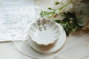 Delicate dangle earrings displayed on a white scalloped dish with soft floral accents and lace details.