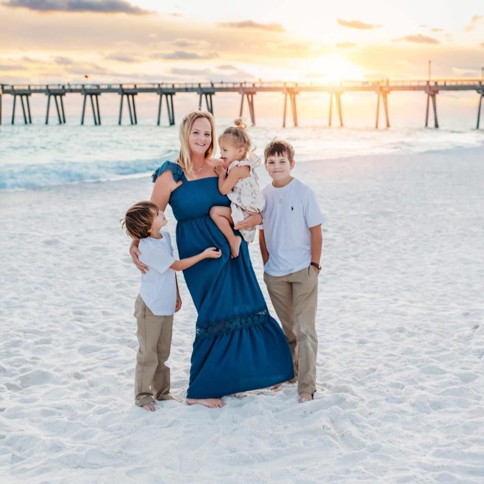 Family portrait session on white sandy beach at sunset with pier in background.