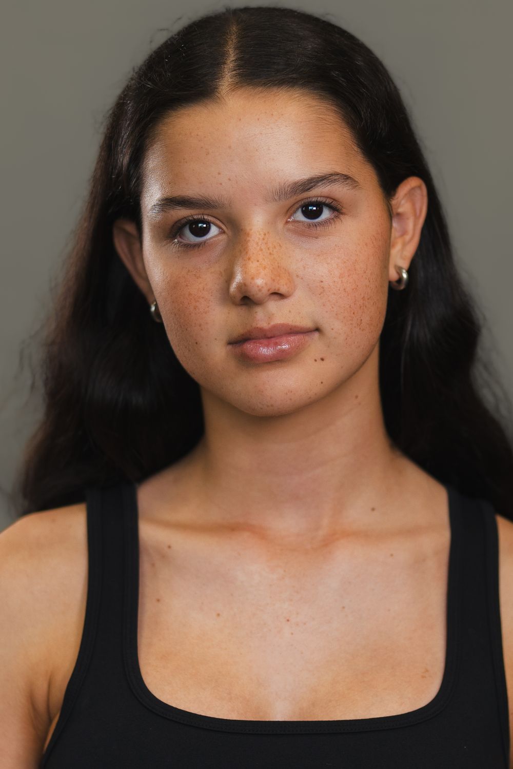 Studio portrait with natural makeup wearing black tank top against grey background.