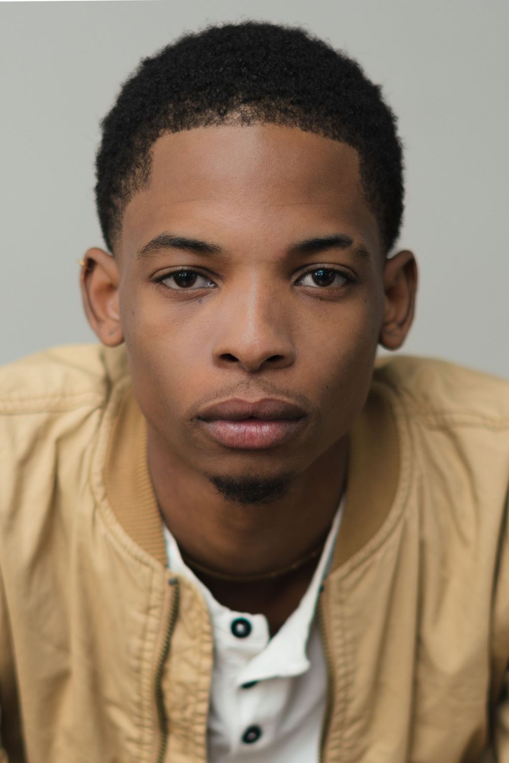 Clean headshot in beige jacket and white henley against neutral background.