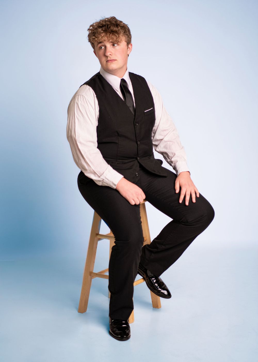 A figure in formal attire sits on a wooden stool against a light blue background in a series of dynamic poses.