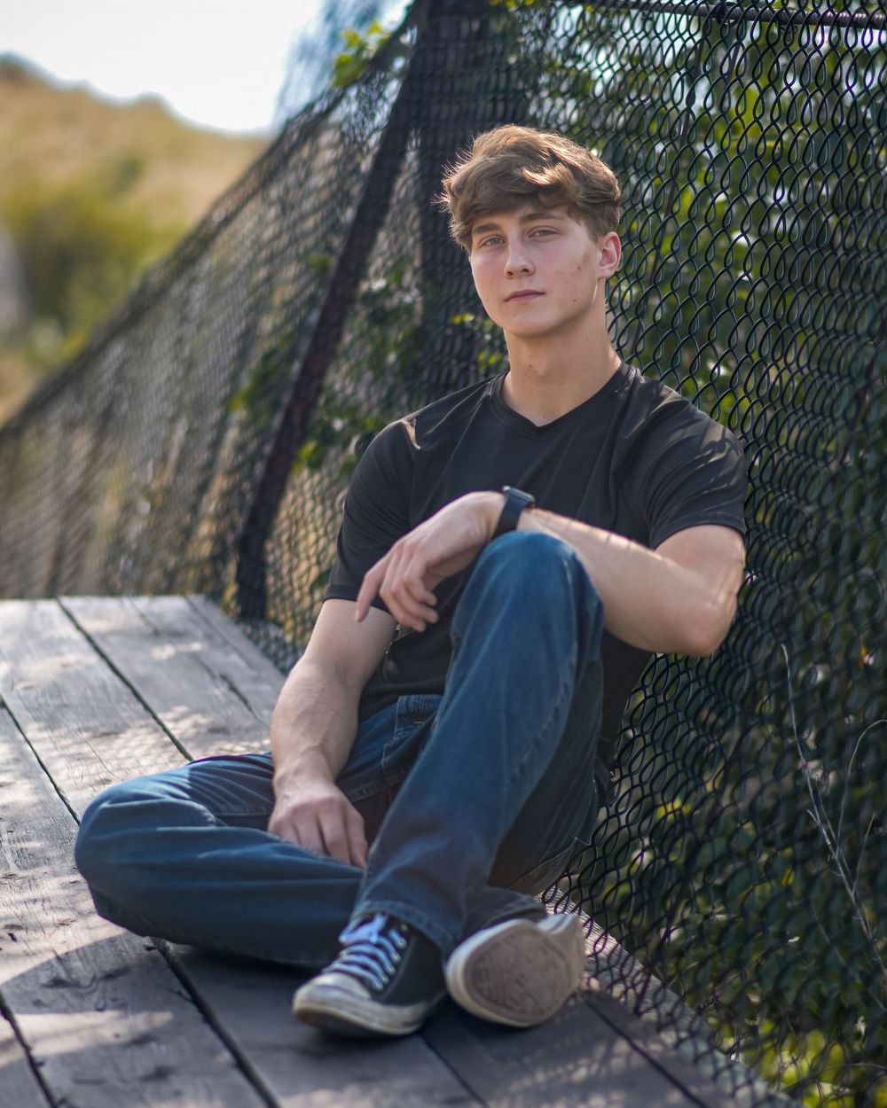 A series of outdoor portrait photographs showing someone lounging against a black fence with ivy growing in the background.