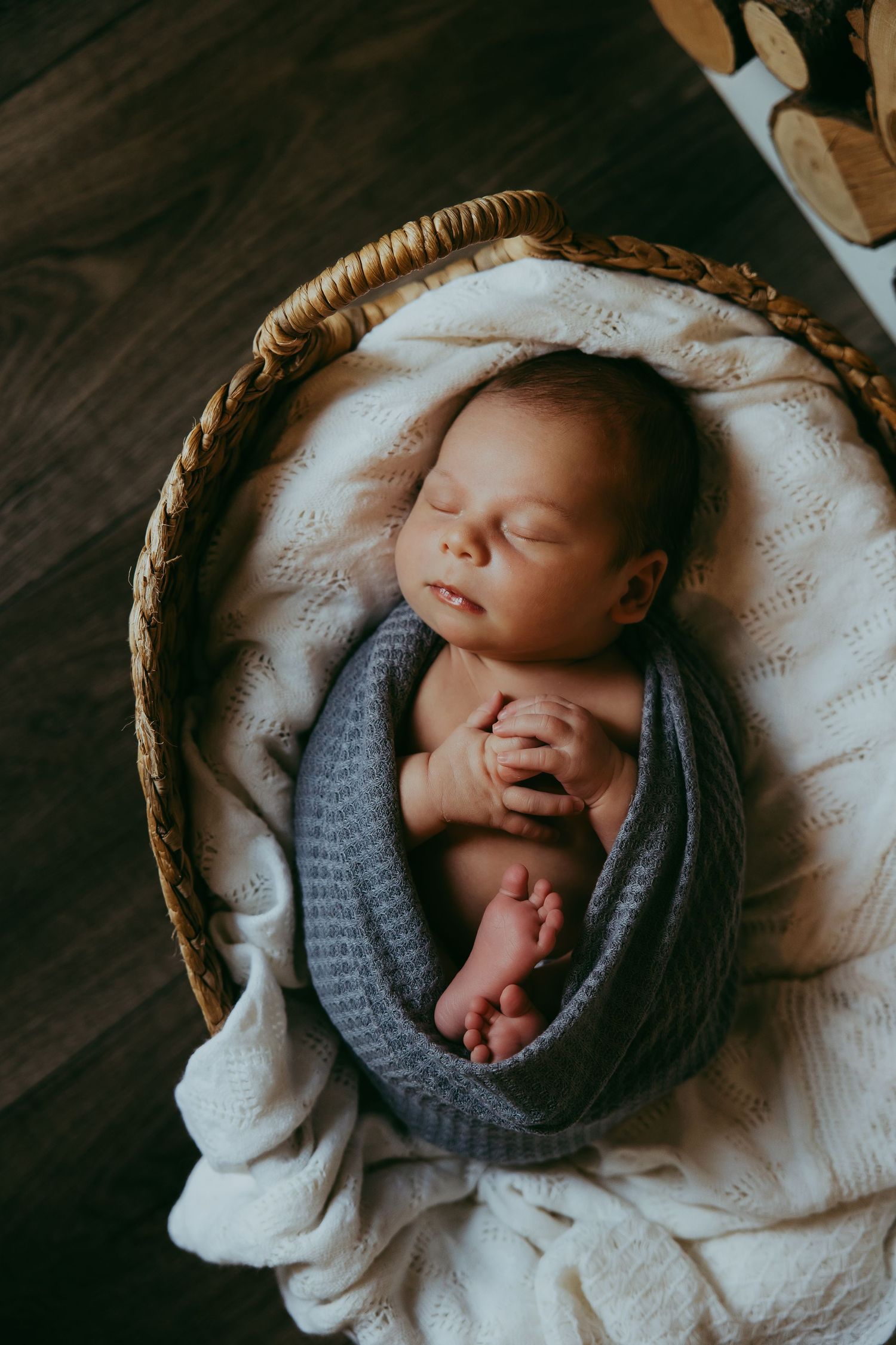 Sleeping newborn wrapped in grey knit blanket in woven basket.