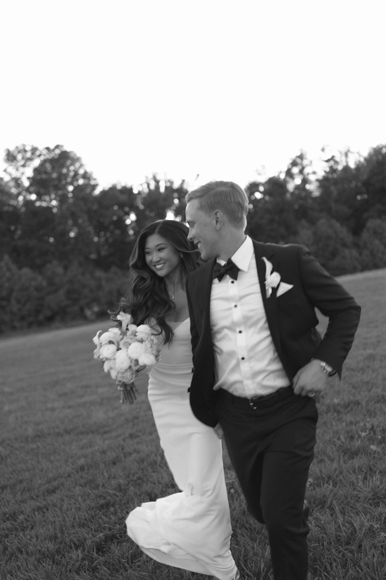 A joyful wedding couple laughs together in a sun-lit field during golden hour.