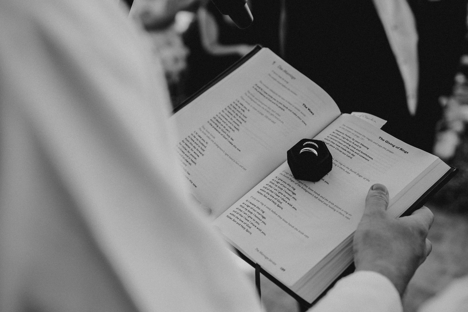 Black and white close-up of wedding rings being exchanged during ceremony.
