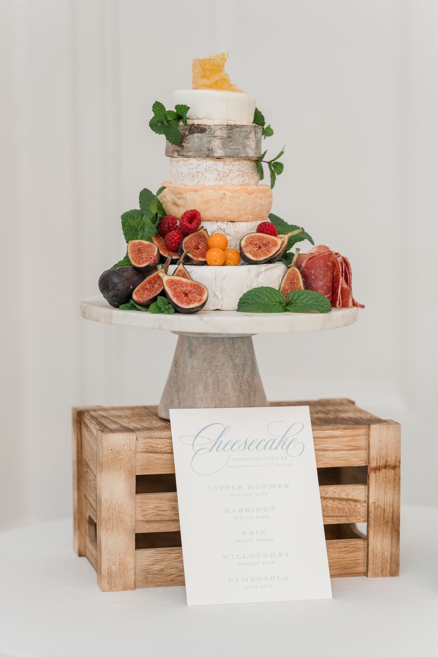Wedding cake decorated with fresh figs and greenery displayed on wooden crates against white backdrop.