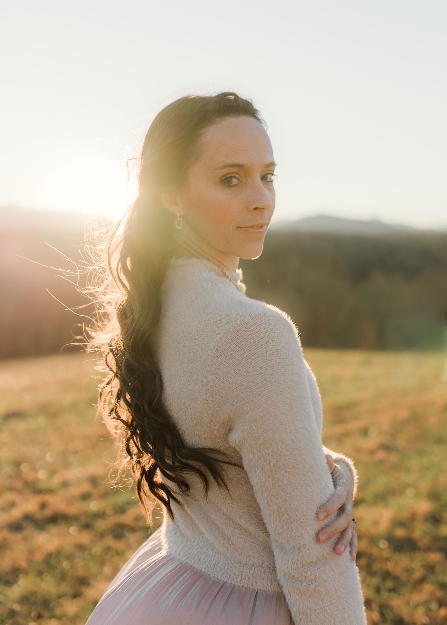 Portrait of a young woman in a sheer polka dot dress with long dark hair and delicate headpiece smiling outdoors.