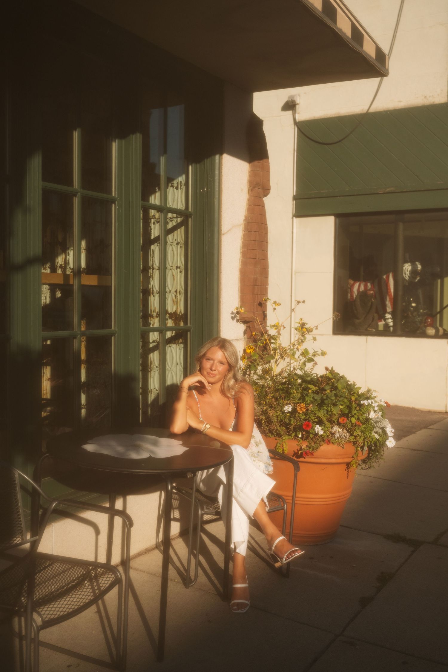 Woman in sage green dress leaning against railing outside modern building at sunset.