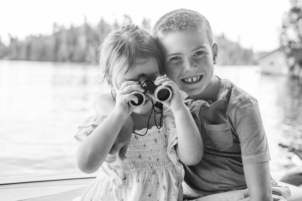 Kids sharing binoculars while sitting together on boat at lake.