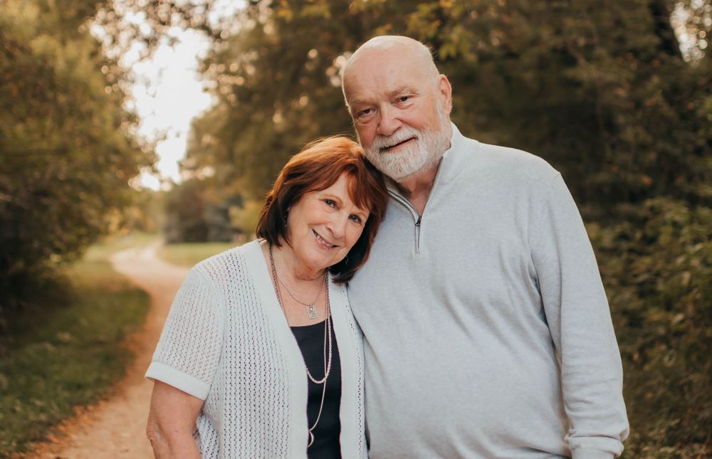 A loving mature couple smiles together on a sunlit path with trees in the background during golden hour.
