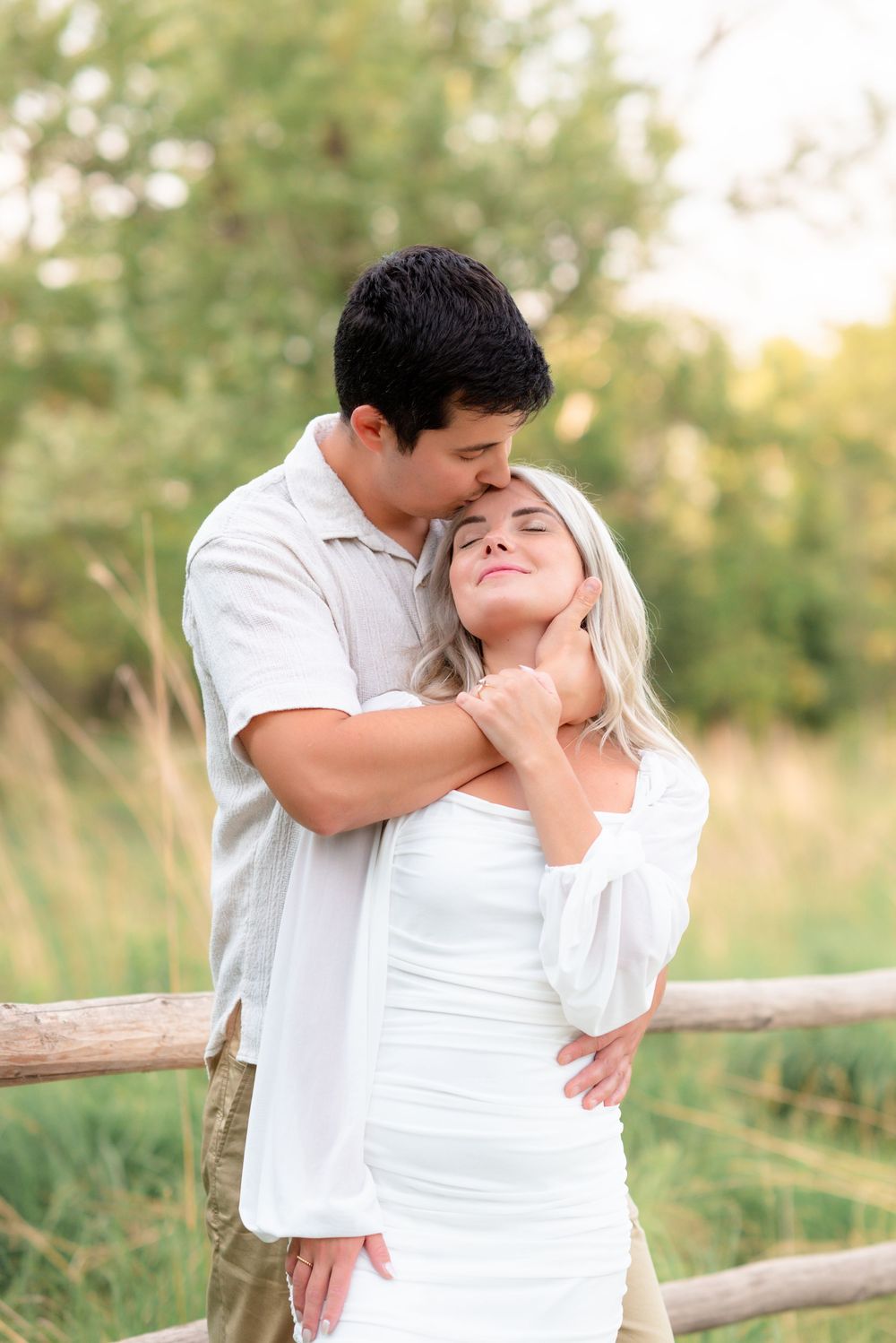 Romantic couple embraces by rustic wooden fence with soft natural lighting in outdoor setting.