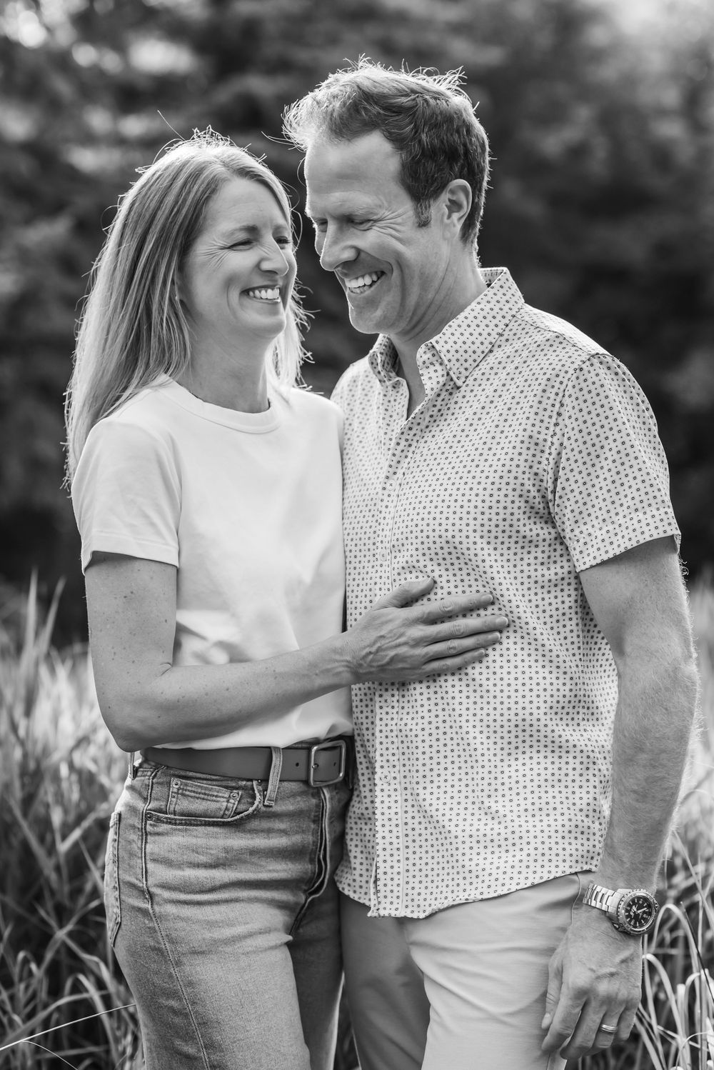 Black and white photo sequence captures a couple sharing joyful laughter together in a natural outdoor setting.