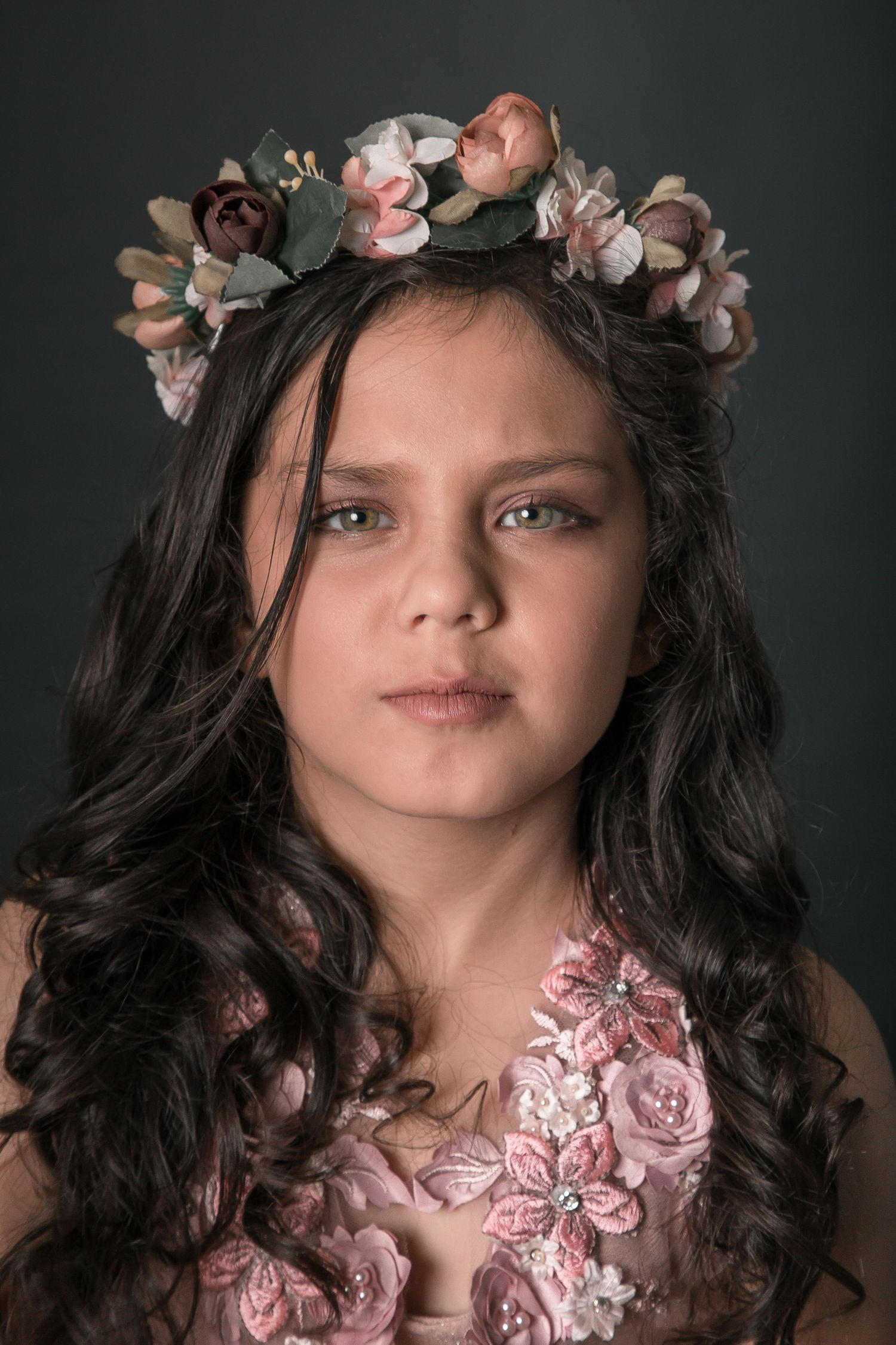 A dreamy portrait of a child in a pink tulle gown and crystal crown against a bokeh backdrop.
